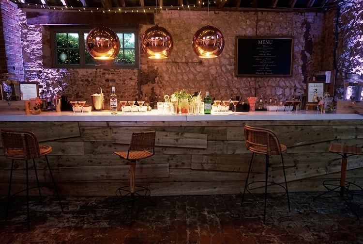 A dressed wooden bar with copper pendant lights in a rustic stone barn