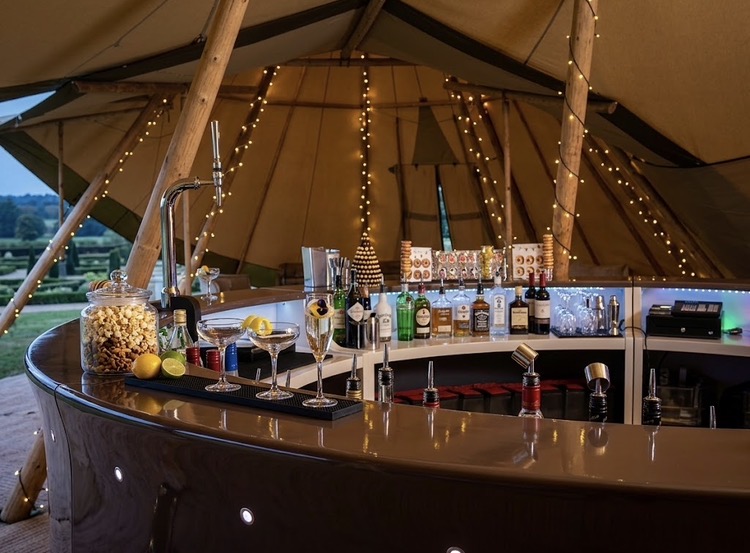Curved mobile bar inside a fairy-lit tipi at an outdoor event