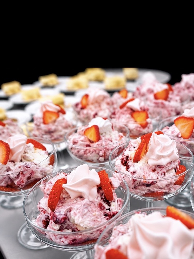 Rows of strawberry Eton mess in glass coupes topped with cream and fresh strawberries