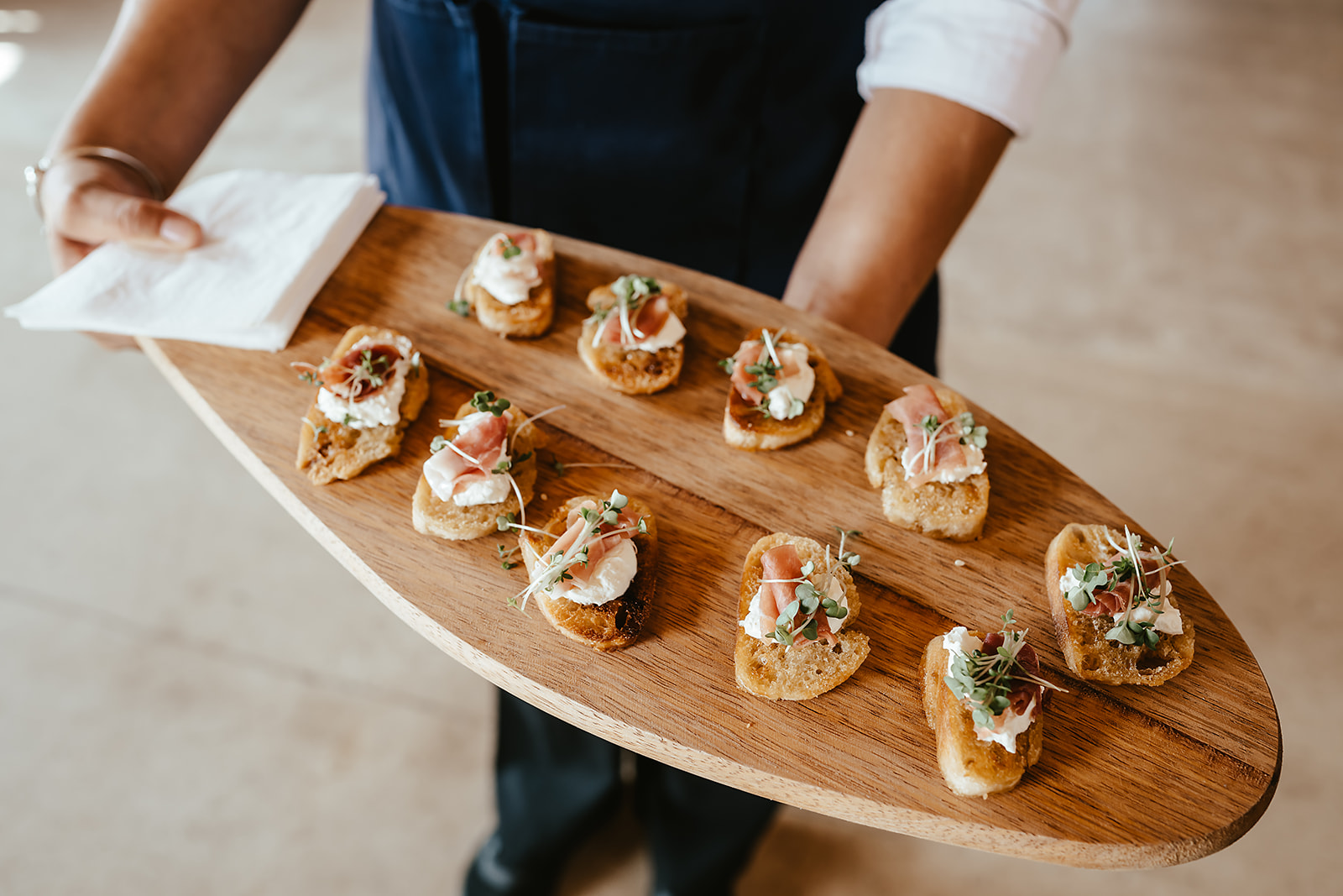 Prosciutto, whipped ricotta and microgreen crostini on a wooden paddle