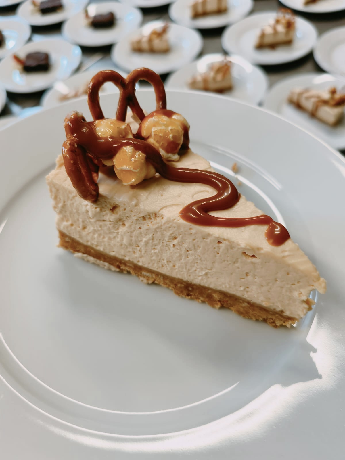 Salted caramel cheesecake slice with pretzel and caramel popcorn, plates lined up behind