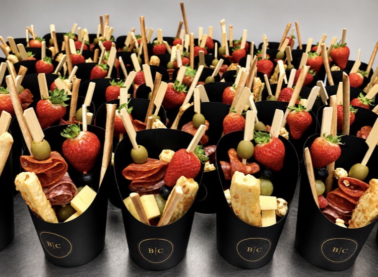 Rows of individual charcuterie cones with salami, cheese, strawberries and grissini