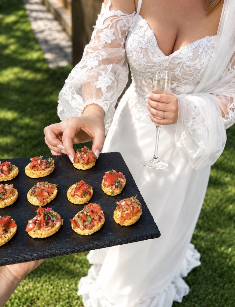 Bride taking a tomato bruschetta canapé from a slate board at a garden drinks reception