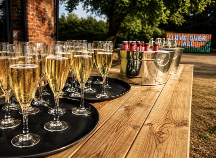 Champagne flutes and bottled beers set out on a garden table at a Norfolk wedding
