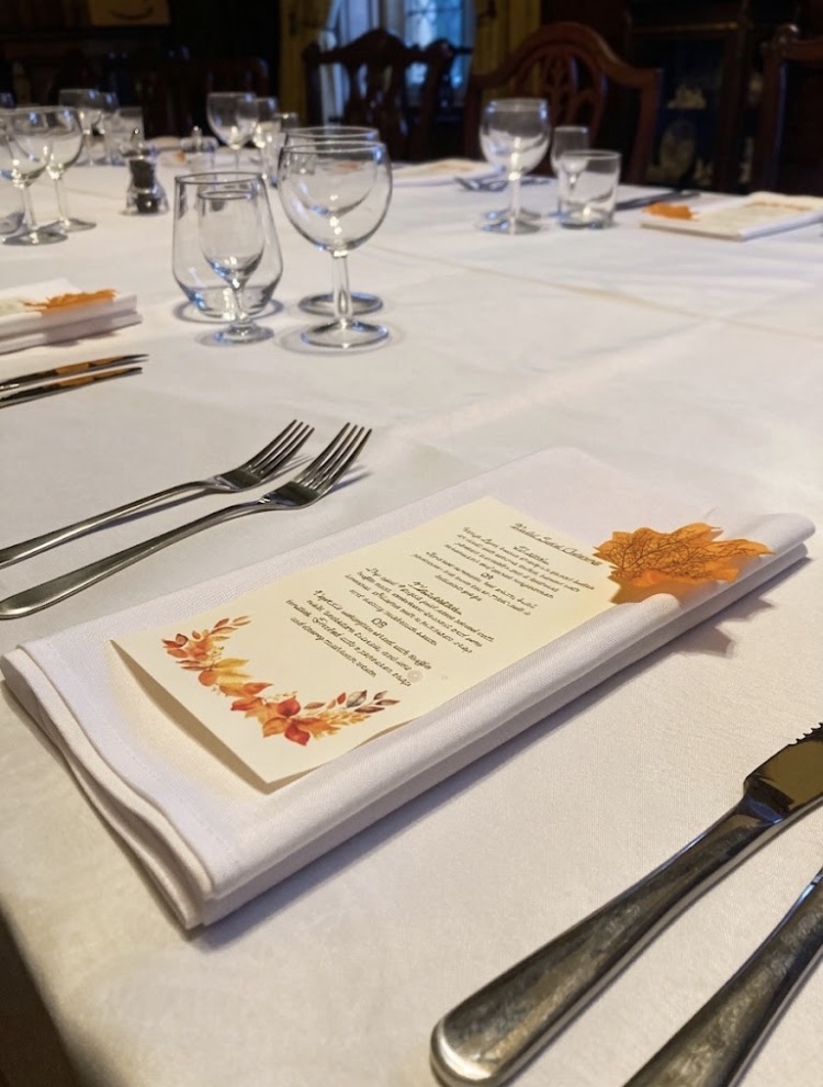 Autumn-illustrated menu card on a folded white napkin at a dressed dining table with polished glassware