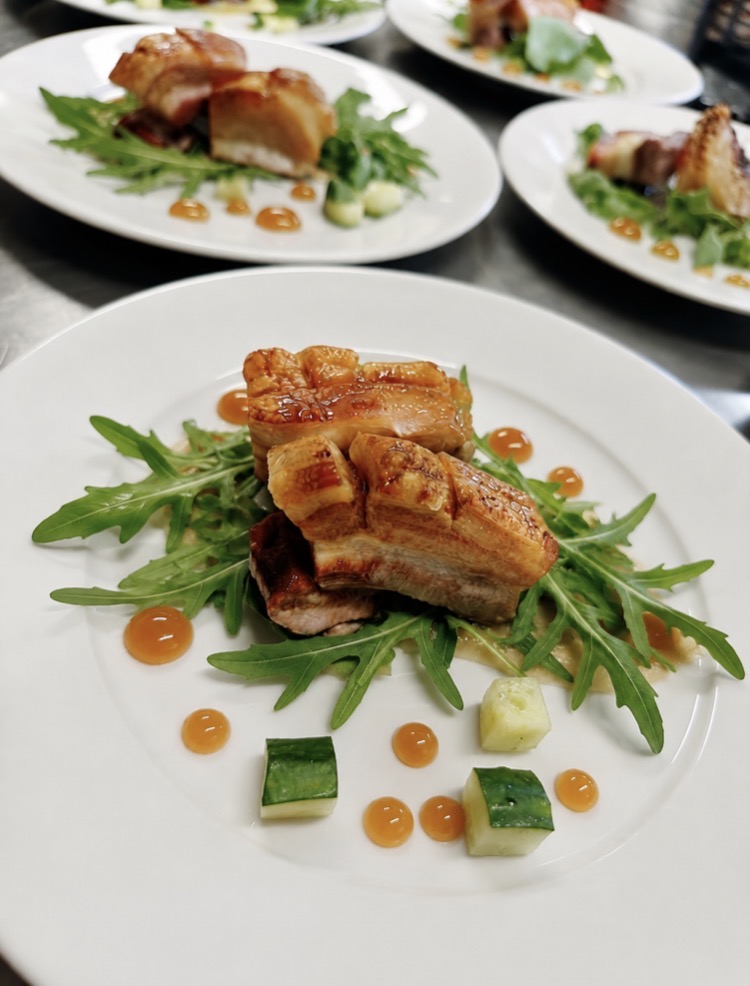 Pork belly starter with rocket, apple purée and cucumber on a white plate