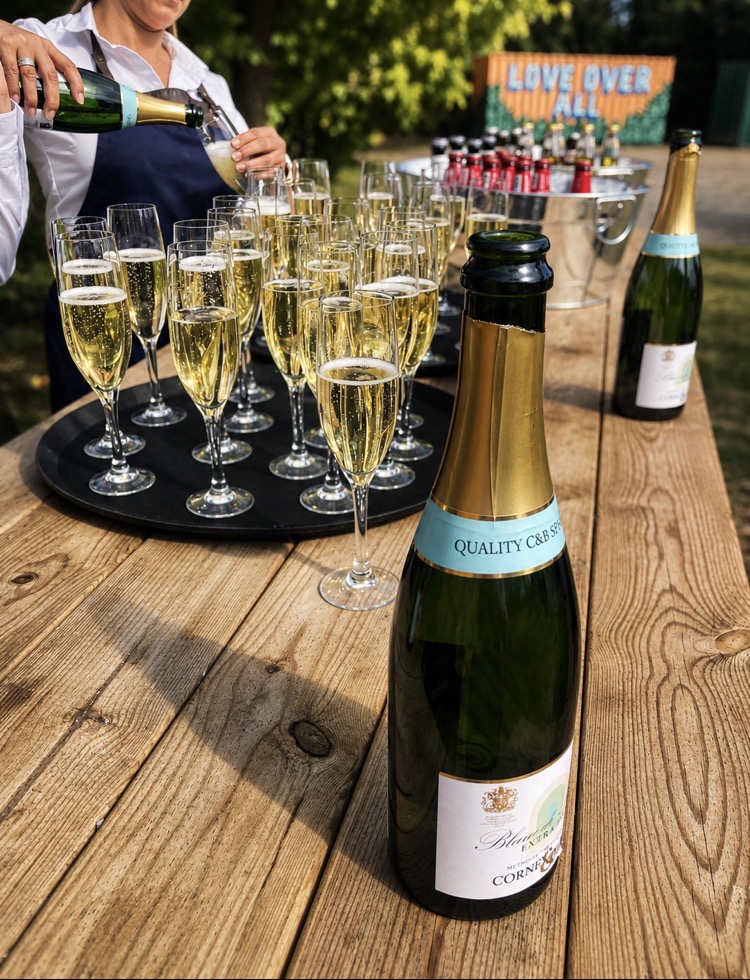 Server pouring sparkling wine into flutes at an outdoor Norfolk wedding reception