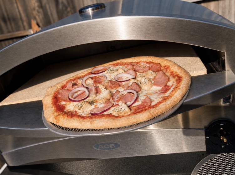 Freshly cooked pizza with ham and red onion coming out of a wood-fired pizza oven