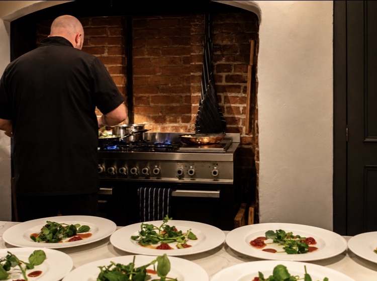 Chef cooking on a range in a brick fireplace with watercress starters plated on the pass