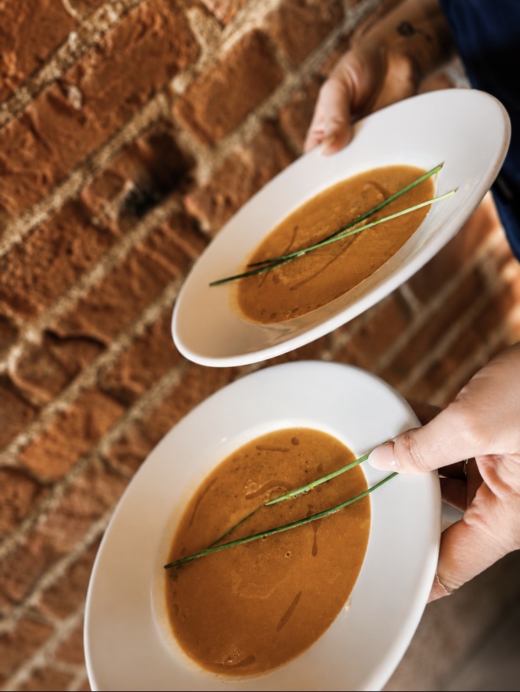 Two bowls of smooth soup garnished with chives, carried against a brick wall