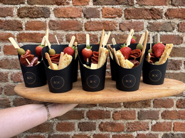 Wooden board of individual charcuterie cones carried against a brick wall
