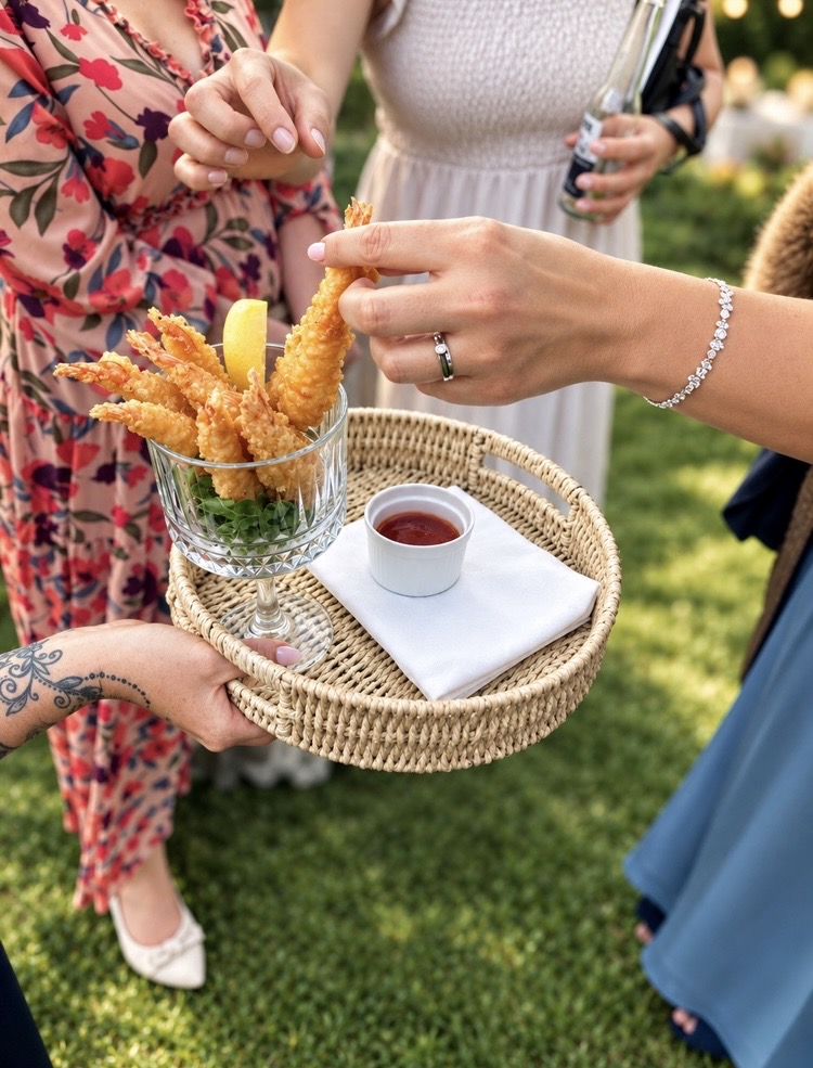 Crispy breaded prawns in a cut-glass coupe with sweet chilli dip on a woven tray at a garden reception