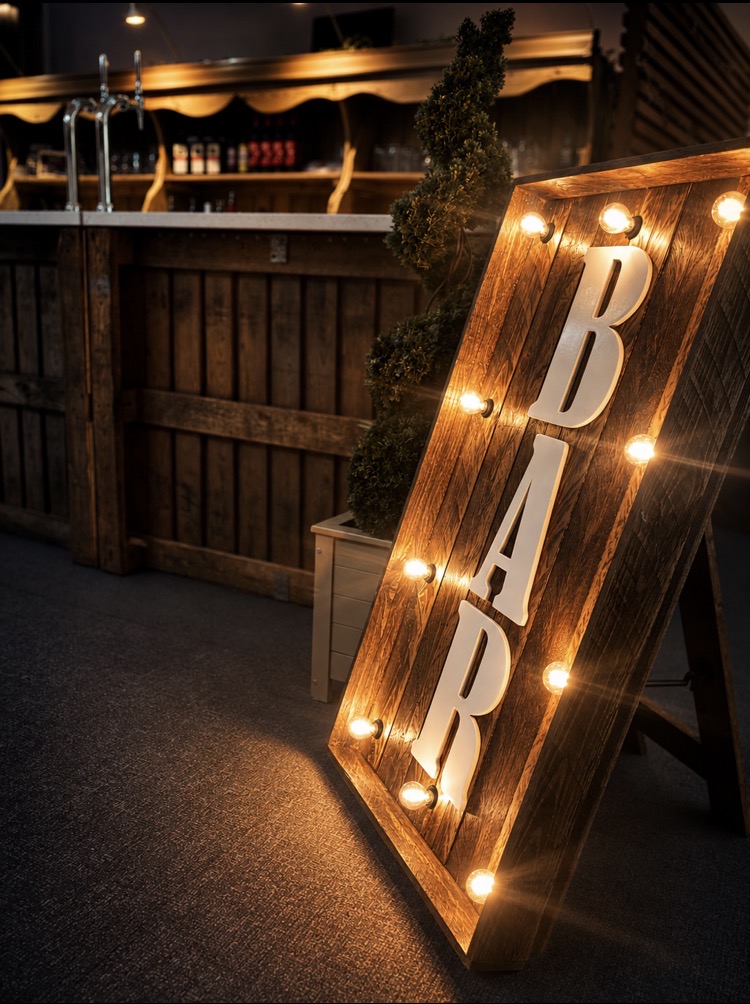 Illuminated rustic wooden bar sign at an evening event near Norwich