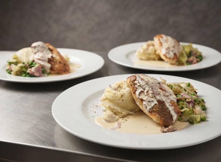 Plated chicken supreme main courses with mash, greens and a creamy bacon sauce on the pass