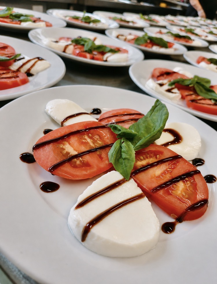 Caprese starters of tomato, mozzarella and basil with balsamic glaze lined up on the pass