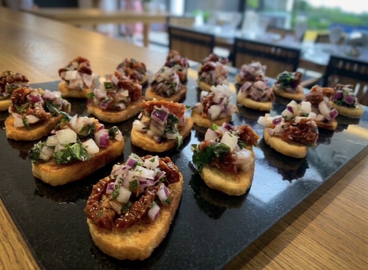 Sun-dried tomato and red onion bruschetta canapés lined up on a slate serving board