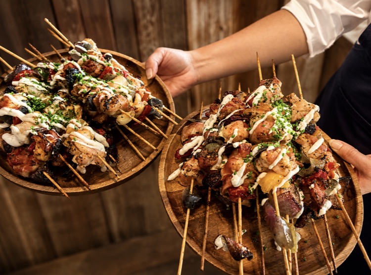 Two wooden boards of grilled chicken and vegetable skewers with herb dressing