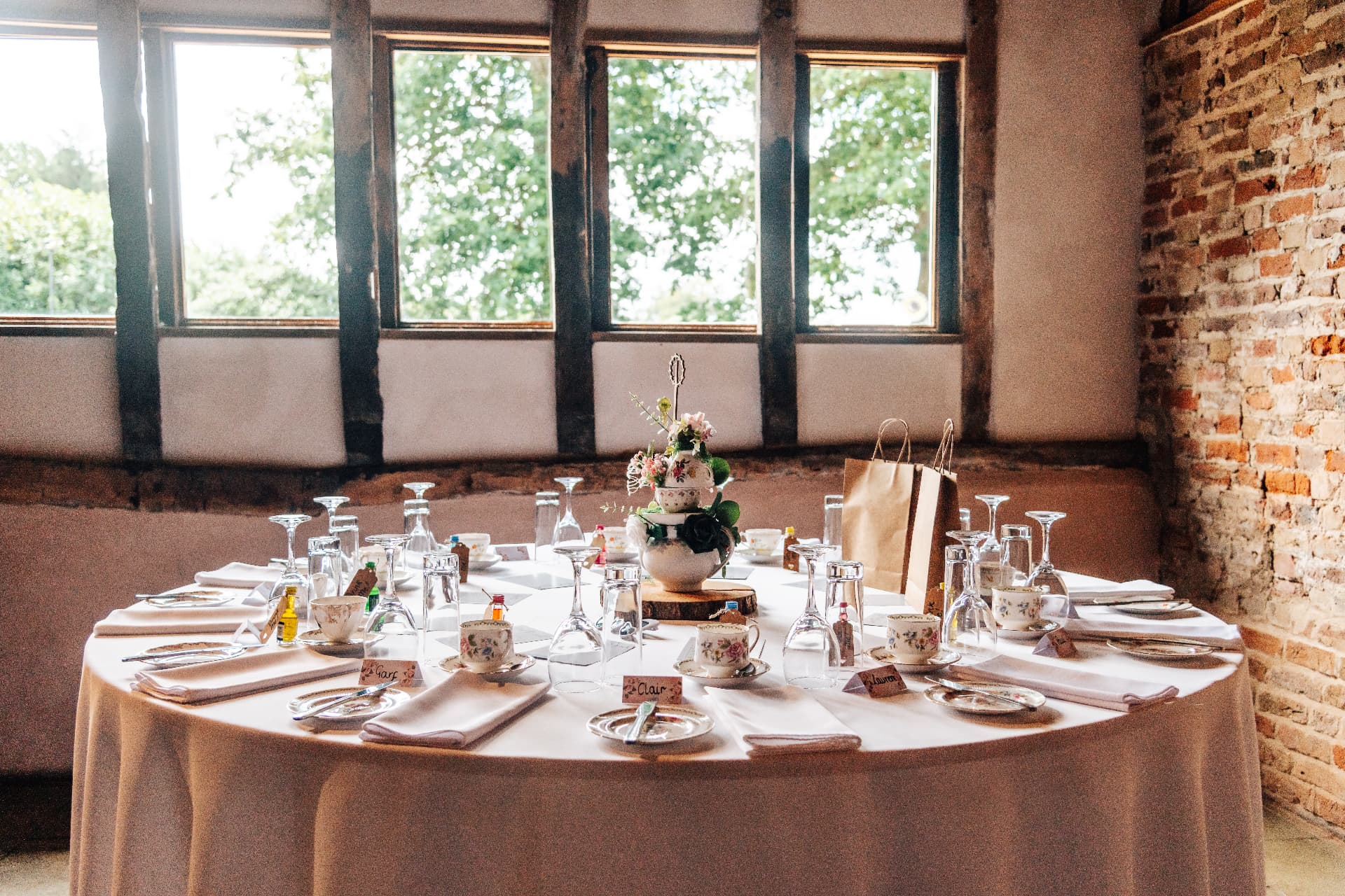 Vintage teacups, place cards and polished glassware on a dressed round table by barn windows